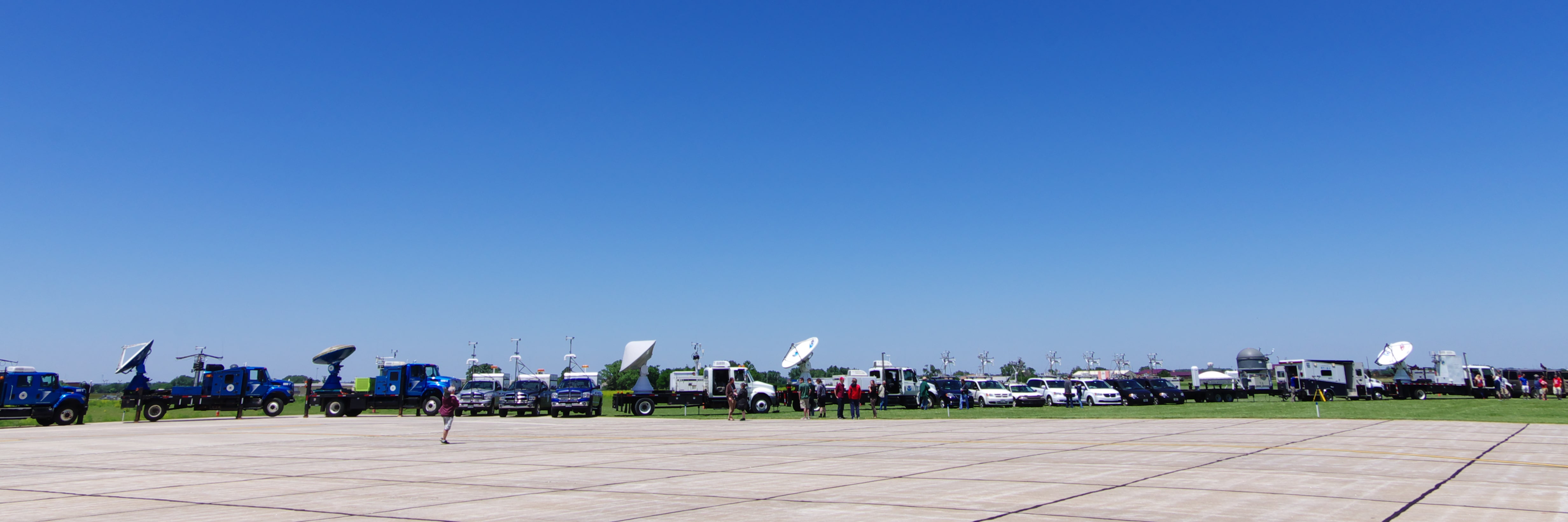 Research Vehicles for the PECAN field experiment are parked in a long row, with an assortment of people standing outside the vehicles.