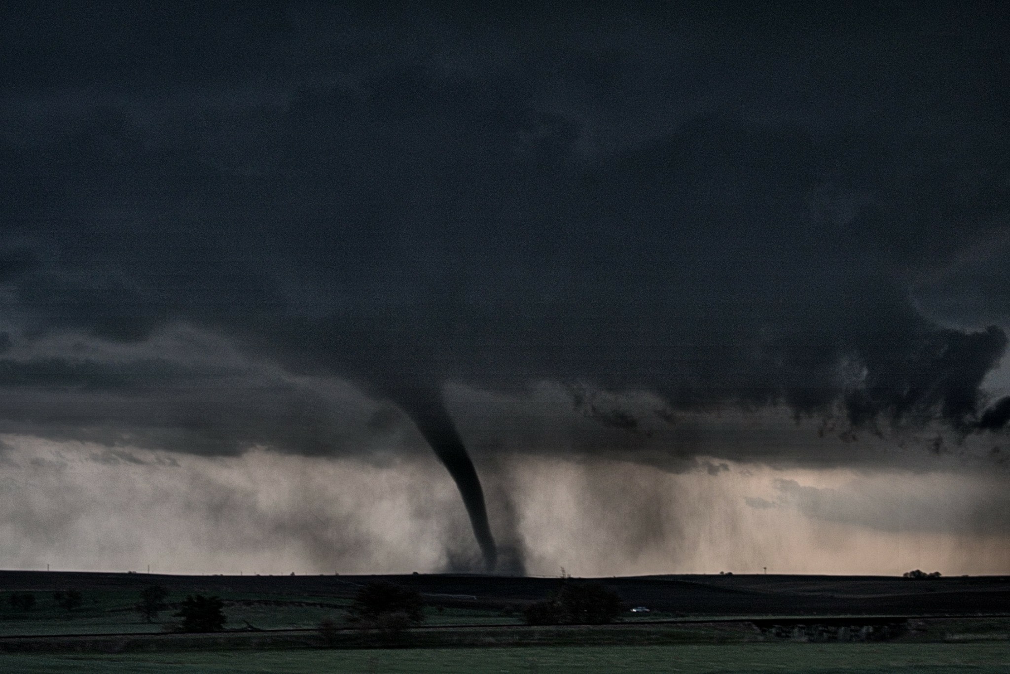 A tornado touching down in a field. | A Person sitting at a table with a computer in front of them. | A group of people gathered around a table having a discussion.